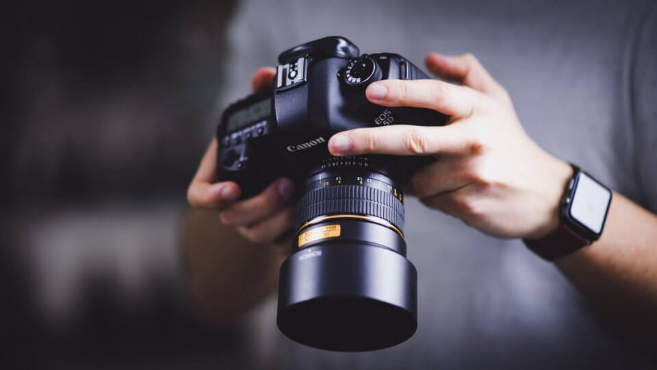 Person holding Canon DSLR camera - William Bayreuther